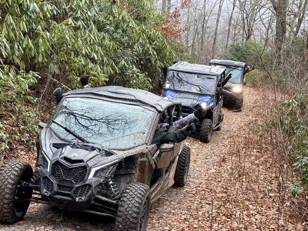 3 UTVs driving up a wooded path
